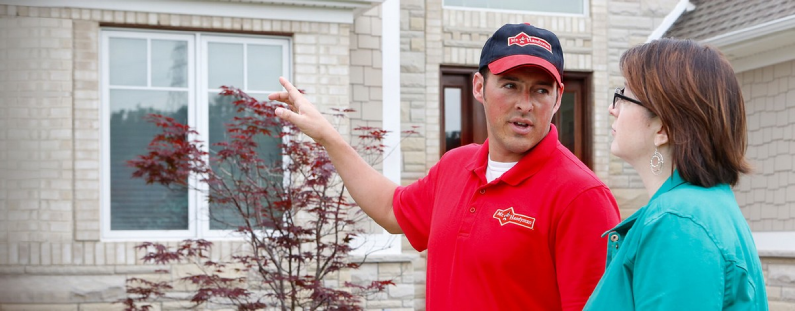 A Mr. Handyman service professional speaking with a client in front of their house.
