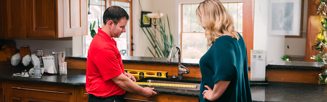 Mr. Handyman professional measuring kitchen sink with customer.