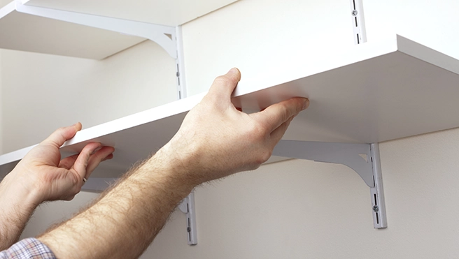 Hands placing shelf on brackets.