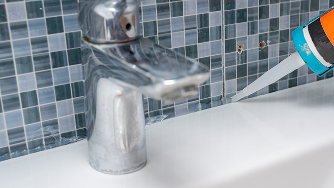 A picture of a caulk bottle caulking around a bathroom sink.