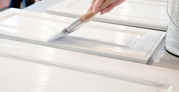 A paintbrush painting a cabinet door white.