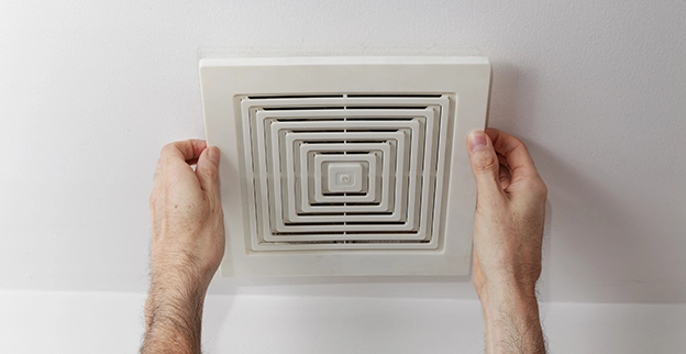 A picture of someone installing an exhaust fan cover.