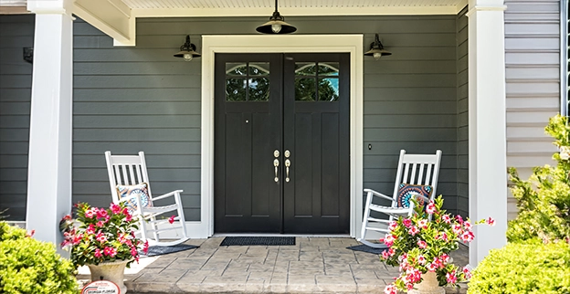 A picture of two rocking chairs aside a large double-handled front door of a home.