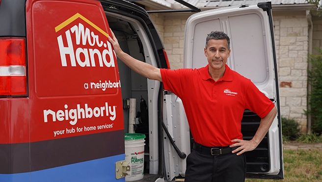 Mr. Handyman tech standing in front of the back of a service van.