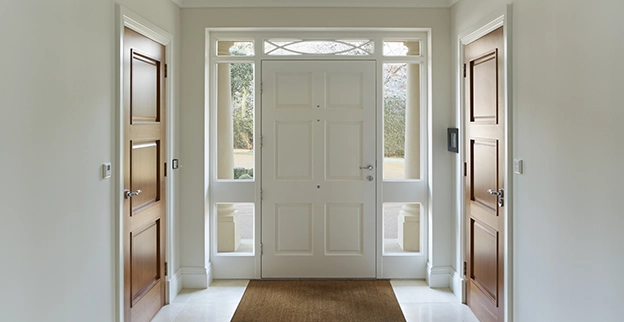 A bright entrance hall featuring a central white door flanked by windows.