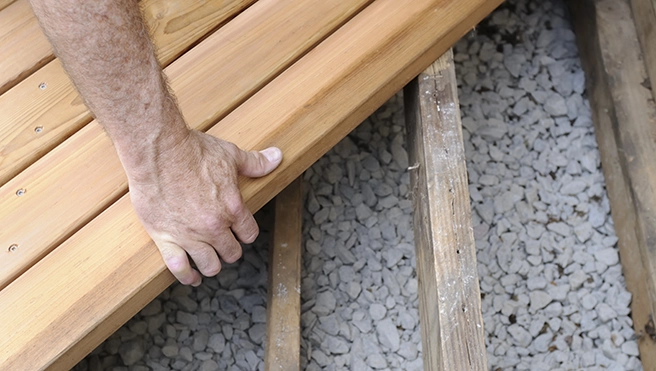 A close-up of a hand placing a wooden plank onto a structure of wooden beams.