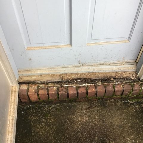 Rotting wood on base of door trim surrounded by brick before repair.