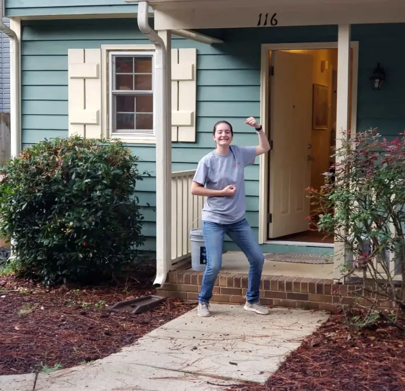 Mr. Handyman technician flexing arm in front of a home.