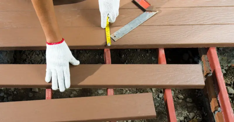 A handyman using a carpenter’s square and a tape measure to lay new deck boards during an appointment for deck repair service.