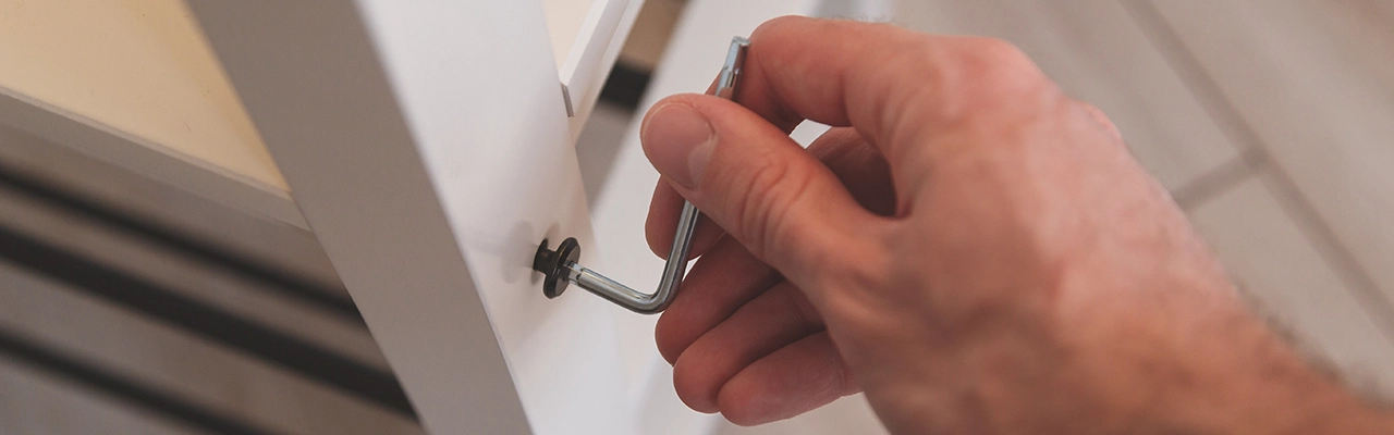 A person using an L-shaped wrench to tighten a bolt on a white furniture piece.