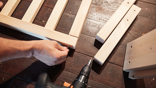 A person uses a drill to assemble wooden pieces on a brown surface.