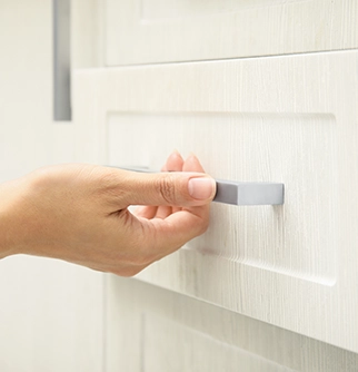 A hand reaching for a sleek, modern cabinet handle on a light-colored wooden cabinet.