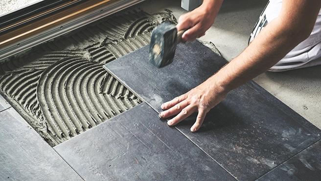 A person installs dark slate tiles, using a rubber mallet.