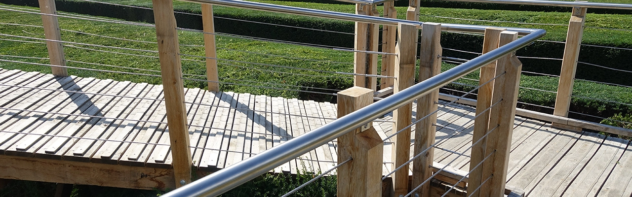 A wooden bridge with metal railing crosses a green landscape.