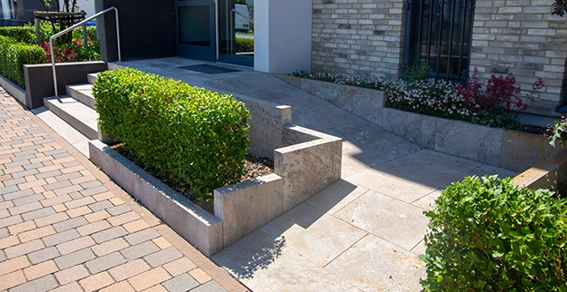 A modern building entrance featuring stone steps and landscaped greenery.