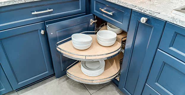 A blue kitchen cabinet with circular pull-out shelves displaying white bowls and plates.