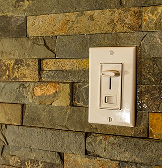 A white light switch mounted on a textured stone wall made of natural slate tiles in earth tones.