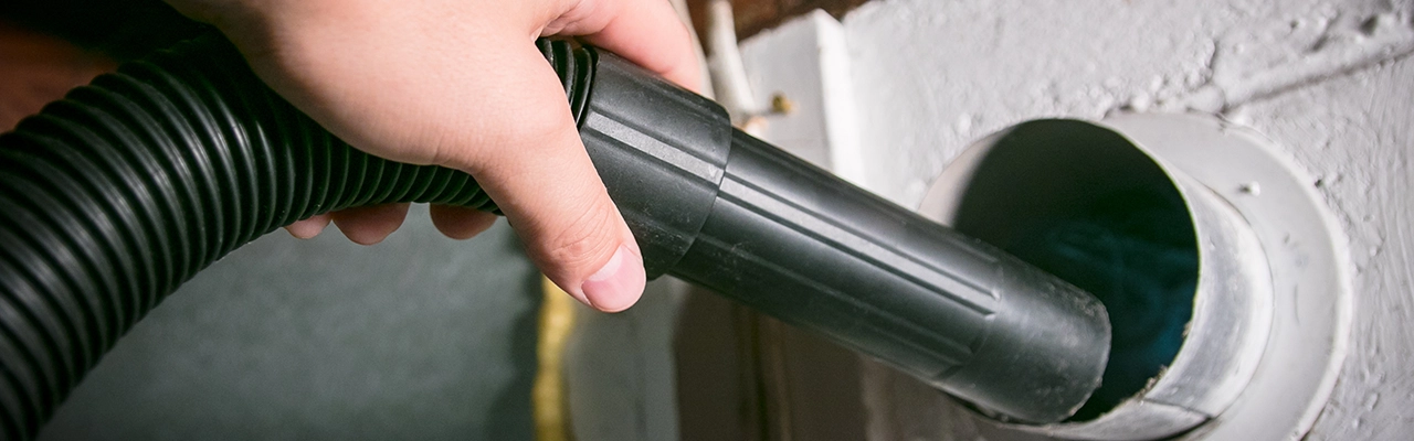 A person holds a black vacuum hose, preparing to connect it to a circular outlet.