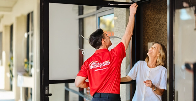 A handyman assists a customer at the entrance gesturing towards the door.