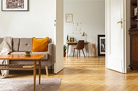 Cozy living room featuring a sofa with an orange cushion, a wooden table, and a view into a work area.