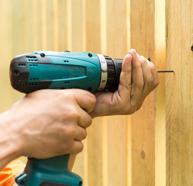 Handyman drilling a hole in wooden wall with a drilling machine.