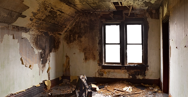 Dilapidated room with peeling paint, scattered debris, and a worn chair, illuminated by two empty windows.
