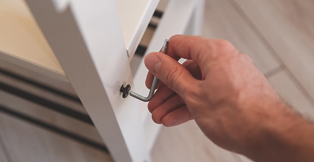 A person uses a tool to assemble a white shelf.