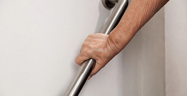 A close-up of hand gripping a metallic handrail mounted on a wall for support.