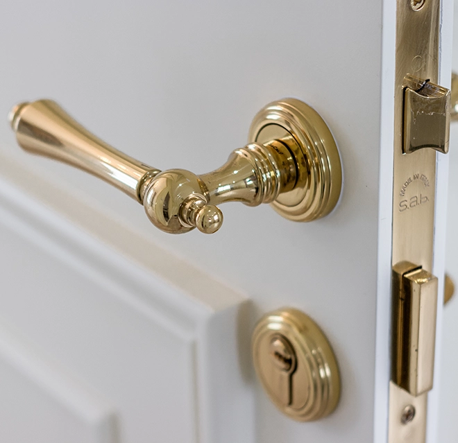 Close-up of a stylish gold door handle and lockset on a white door.