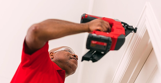 A man uses a power nailer to fasten trim to the wall.