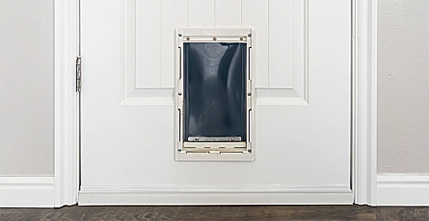 A white door featuring a small pet door cutout, framed in beige, with a black flap.