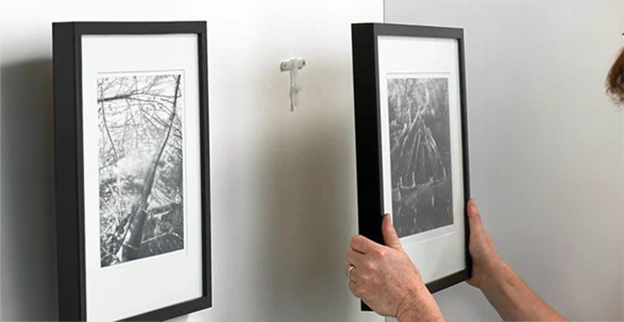 A person hangs two black-and-white framed photographs on a wall.