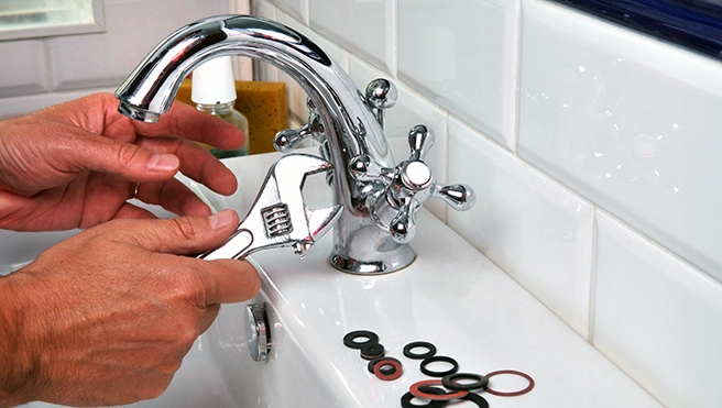 A person using a wrench to repair a chrome faucet.