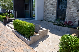 A modern entrance featuring a smooth stone pathway, lush green hedges, and elegantly designed steps.