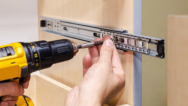A person uses a power drill to install a metal drawer.