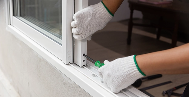 A person wearing gloves tightens screws on a window frame with a screwdriver.