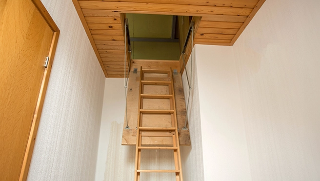 A wooden ladder leads to an attic opening with a wooden ceiling.
