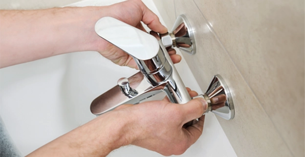 A person installing a modern chrome bathtub faucet.