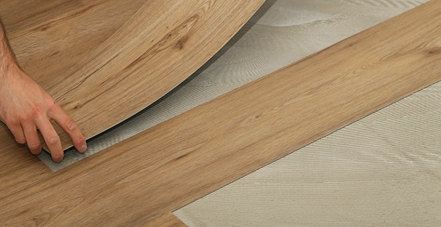 Handyman lifts a laminate flooring plank beneath on a wooden floor surface.