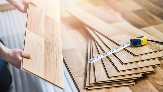 A handyman holding a wooden flooring plank.