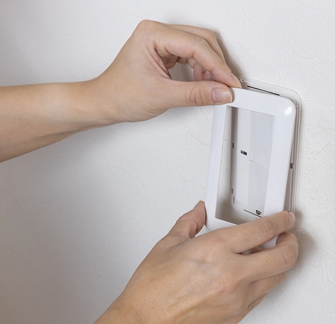 A person installing a white wall-mounted device.