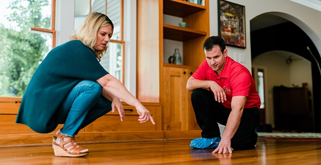 A woman points out something on a wooden floor while a man inspects it closely.