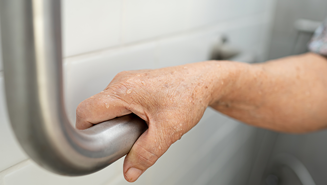 An elderly hand gripping a metallic grab bar, showcasing details like wet skin