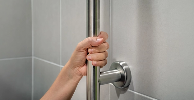 A hand grasping a silver grab bar mounted on a tiled wall.