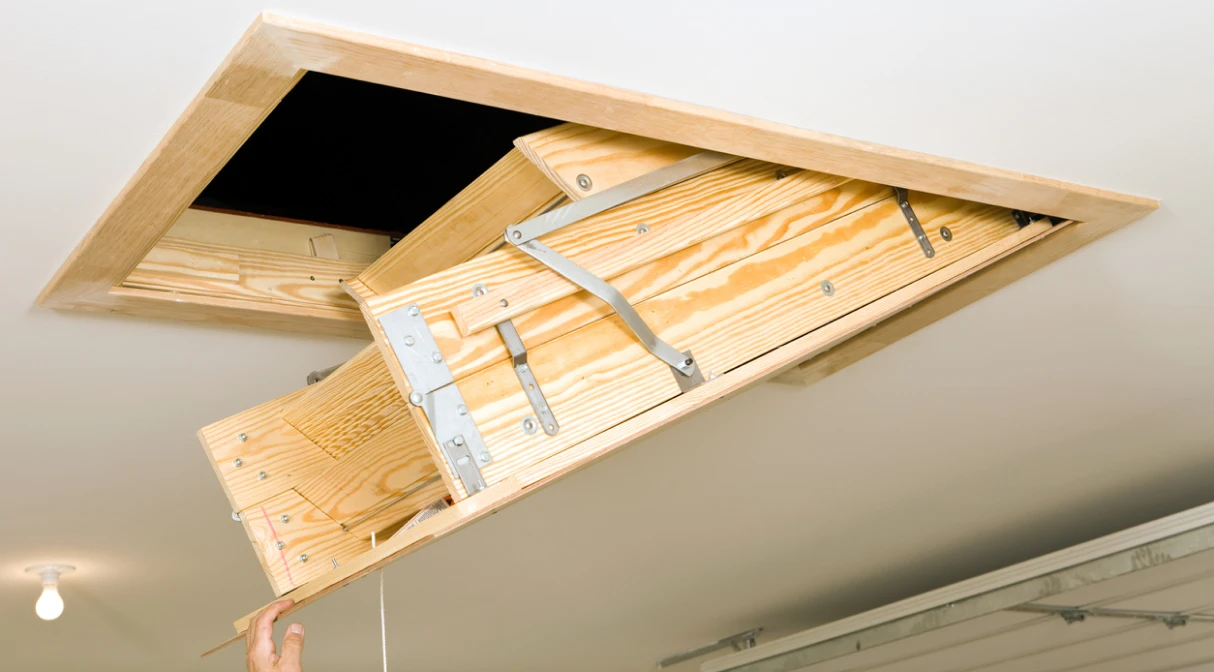 A set of attic stairs being closed into the ceiling.