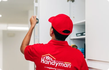 A Mr. Handyman service professional using a level on a cabinet door.