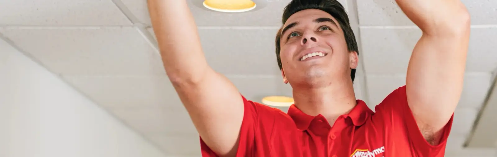 A handyman reaching upward to fix a white tiled ceiling.
