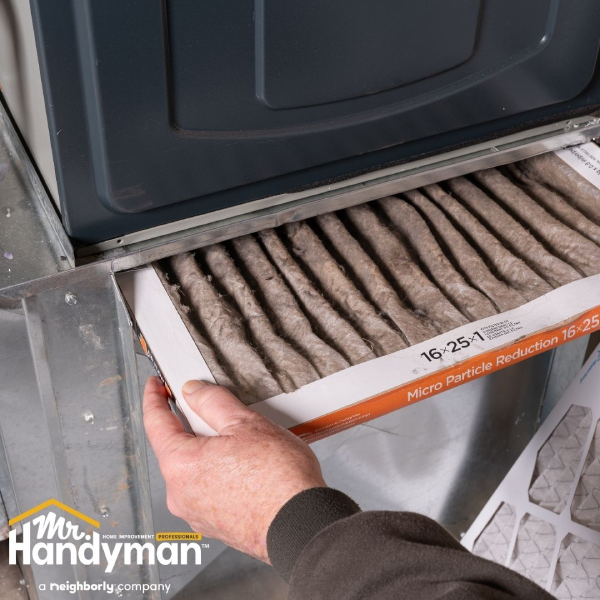 Person sliding out a dirty air filter from a home furnace unit.