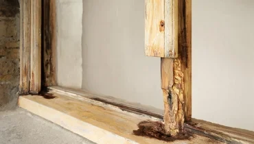 The bottom section of a wooden window frame with several areas damaged by moisture and wood rot.