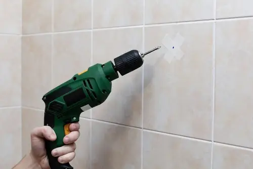 Drilling into tile with painter’s tape to prevent cracking during towel rack installation.